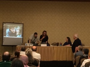 Colin Baker is the older, white-haired gentleman off to the side... and the curly-haired man in leather on the screen.